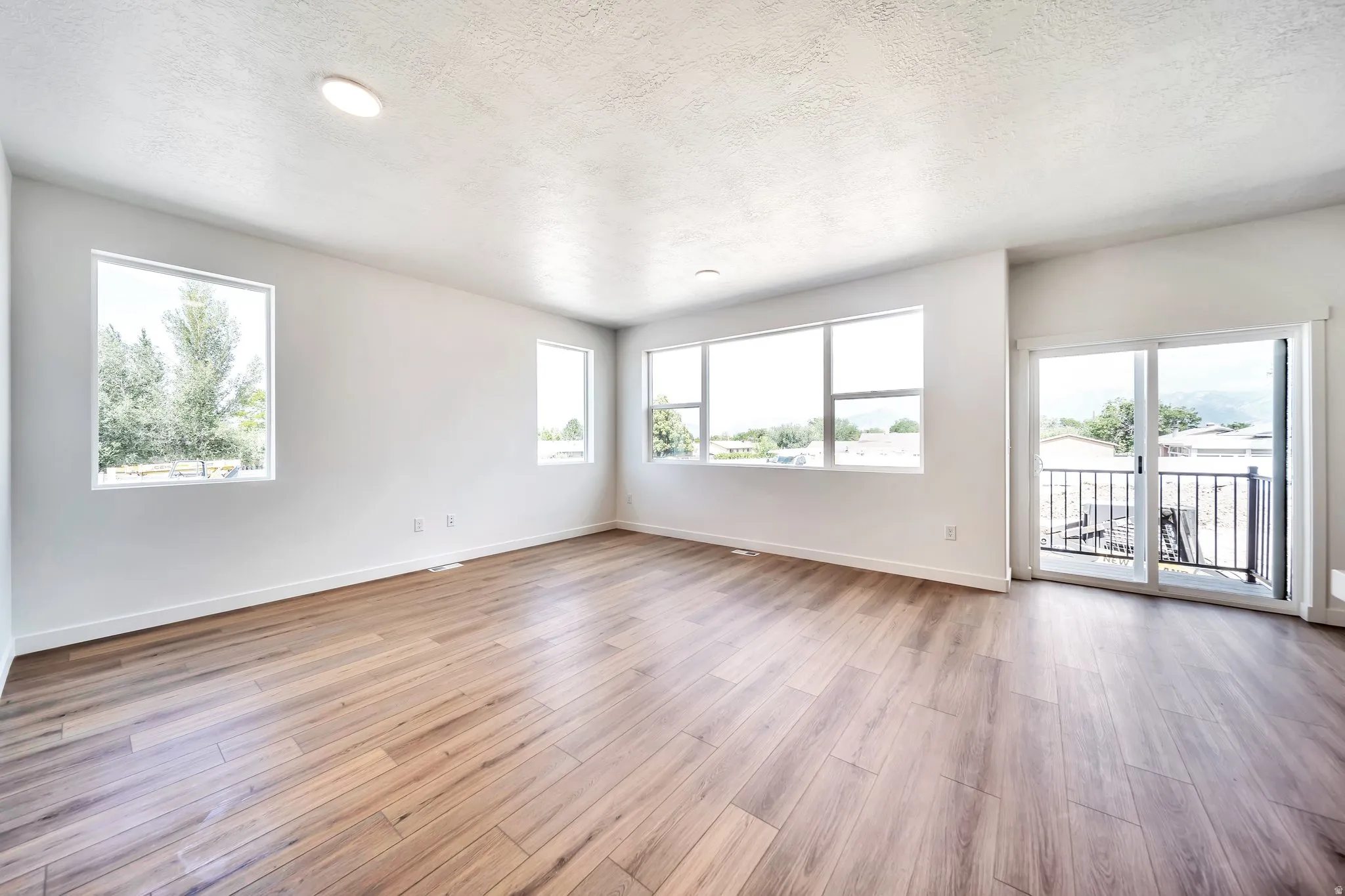 Unfurnished room featuring light wood finished floors, healthy amount of natural light, and a textured ceiling