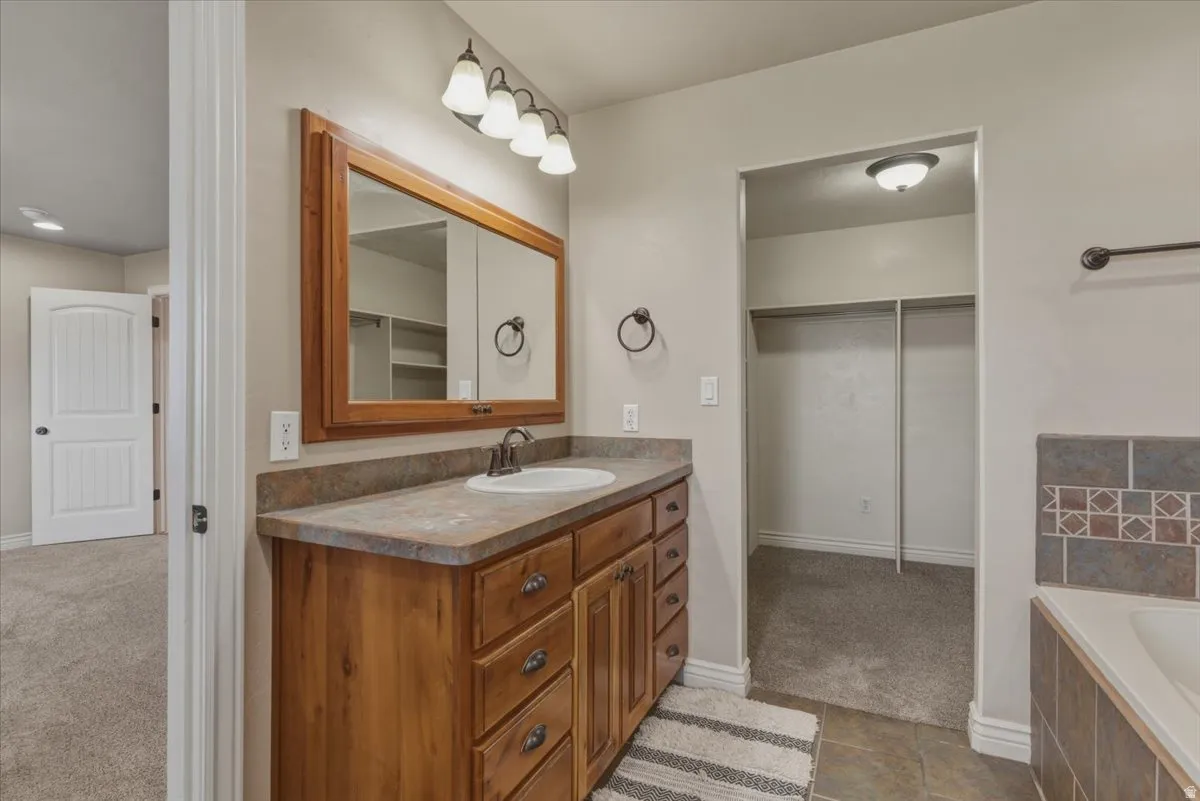 Bathroom featuring vanity, dark carpet, a walk in closet, and a garden tub