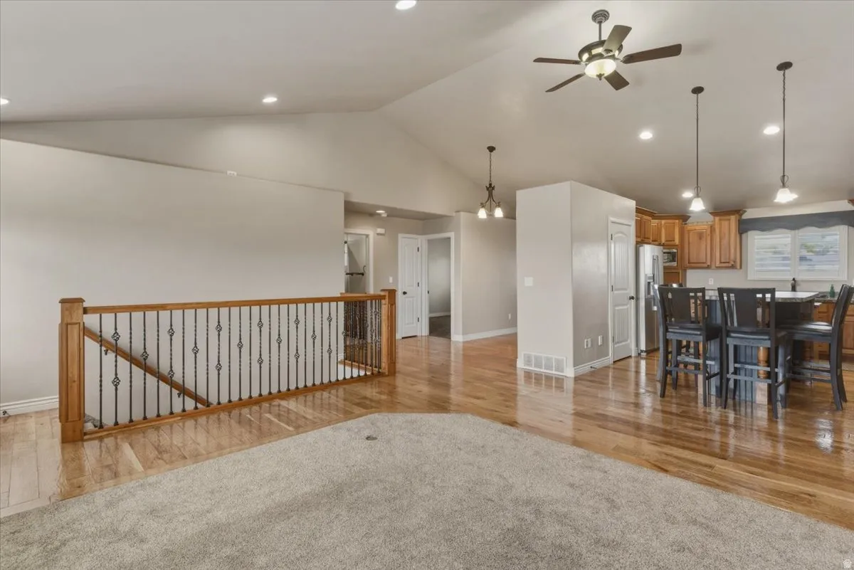 Living room with light wood finished floors, light carpet, a ceiling fan, hanging lights, and a high ceiling