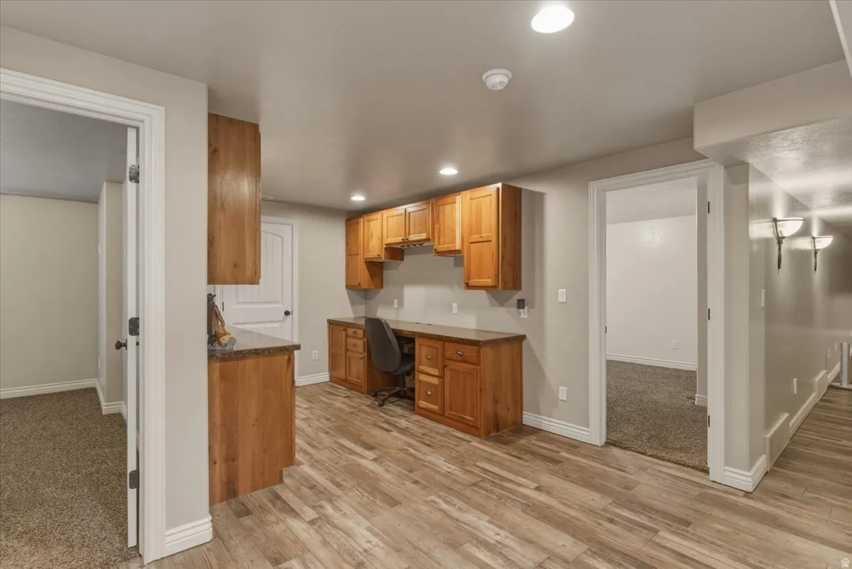 Kitchen with built in desk, dark countertops, light wood-style flooring, wood finish cabinetry, and recessed lighting