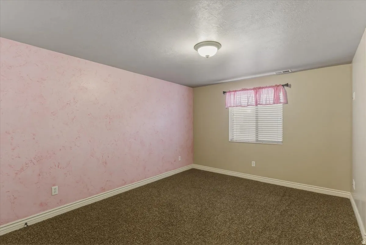 Empty room with wallpapered walls, dark colored carpet, and a textured ceiling
