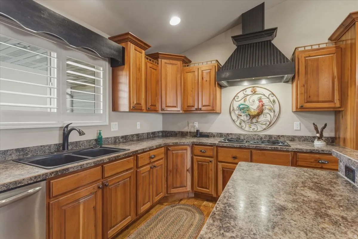 Kitchen featuring ventilation hood, stainless steel appliances, wood finish cabinets, vaulted ceiling, and dark stone countertops