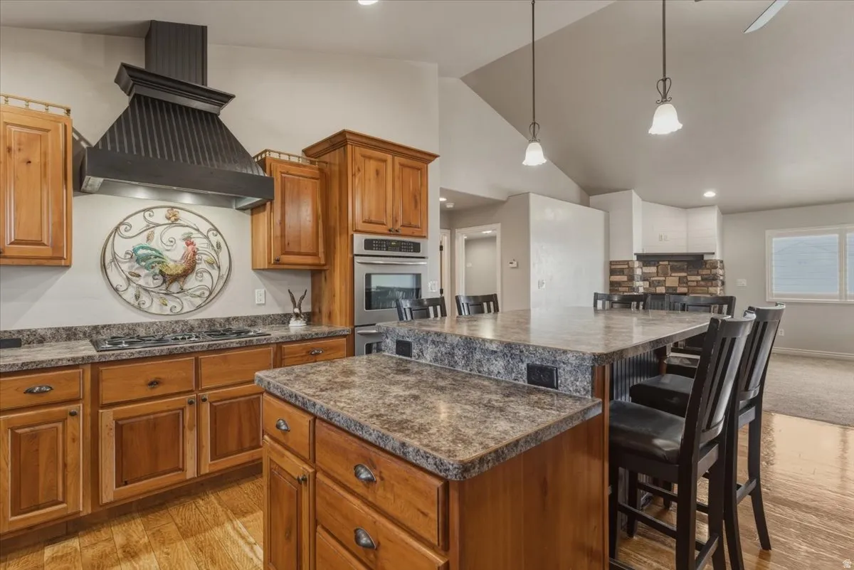 Kitchen with a kitchen island, wood finish cabinetry, a kitchen bar, lofted ceiling, and light wood-style floors
