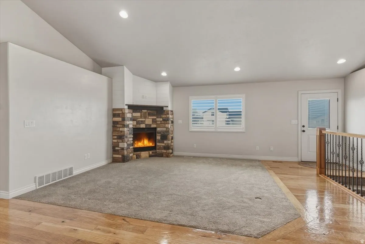 Unfurnished living room with light wood-style floors, a stone fireplace, recessed lighting, light carpet, and vaulted ceiling
