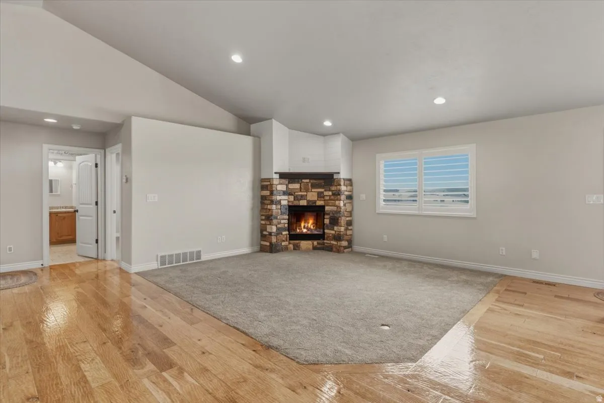 Unfurnished living room featuring vaulted ceiling, light wood-style flooring, a stone fireplace, and recessed lighting