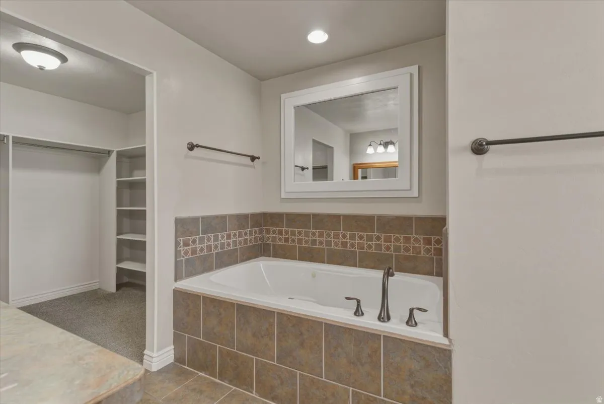 Bathroom with a spacious closet, a bath, dark tile patterned floors, recessed lighting, and vanity