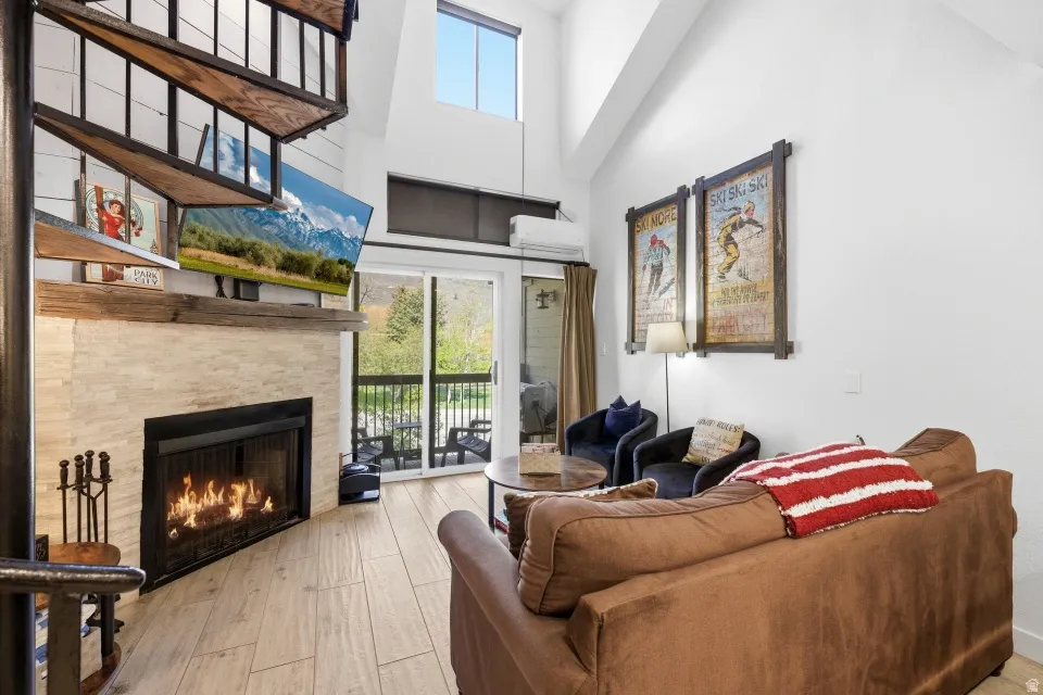 Living room featuring light wood-type flooring, a warm lit fireplace, and a high ceiling