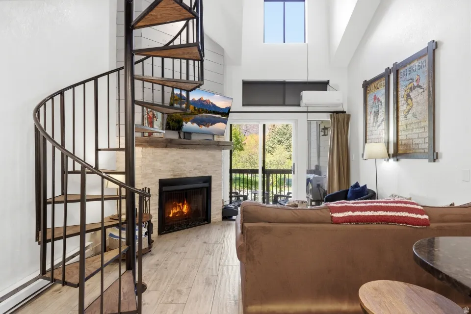 Living room with a warm lit fireplace, light wood-style flooring, a high ceiling, and a baseboard radiator