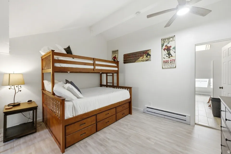 Bedroom with baseboard heating, vaulted ceiling with beams, light wood-style floors, and a ceiling fan