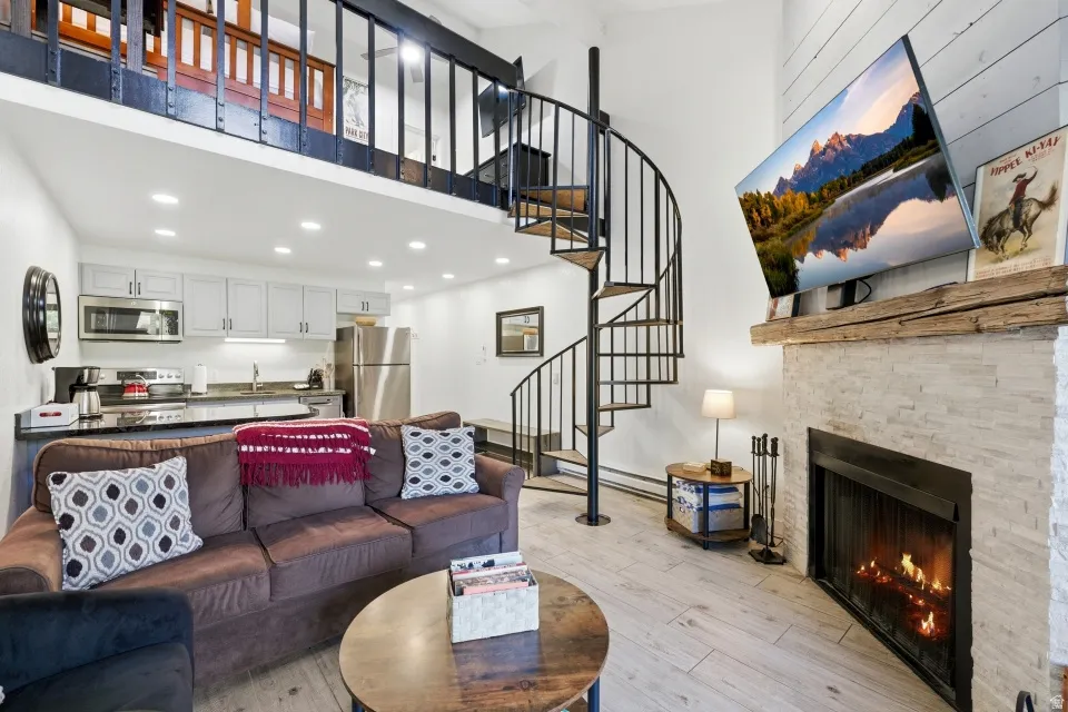 Living area with a fireplace, light wood-style flooring, recessed lighting, and a high ceiling
