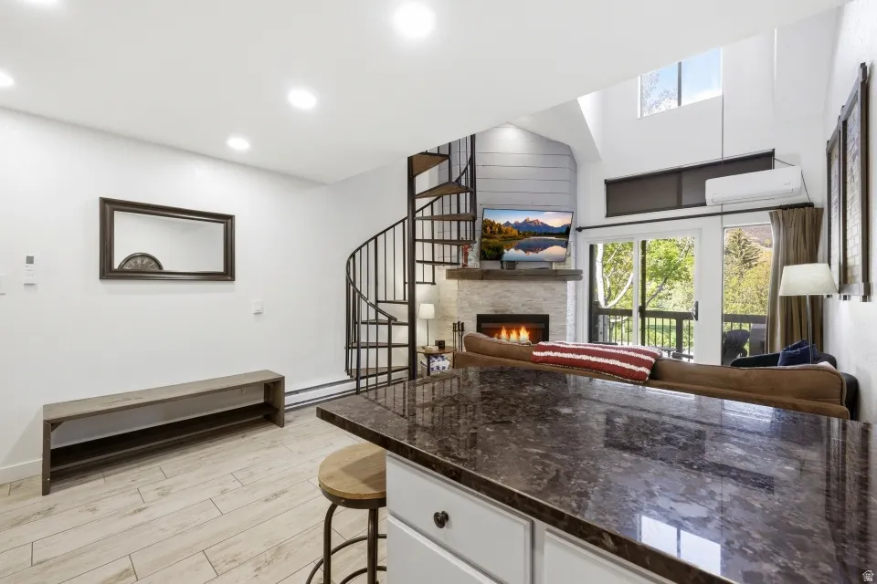 Kitchen with open floor plan, a stone fireplace, light wood finished floors, a kitchen breakfast bar, and white cabinets