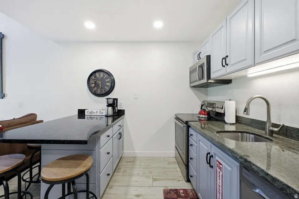 Kitchen with a peninsula, a breakfast bar area, dark stone counters, stainless steel appliances, and recessed lighting