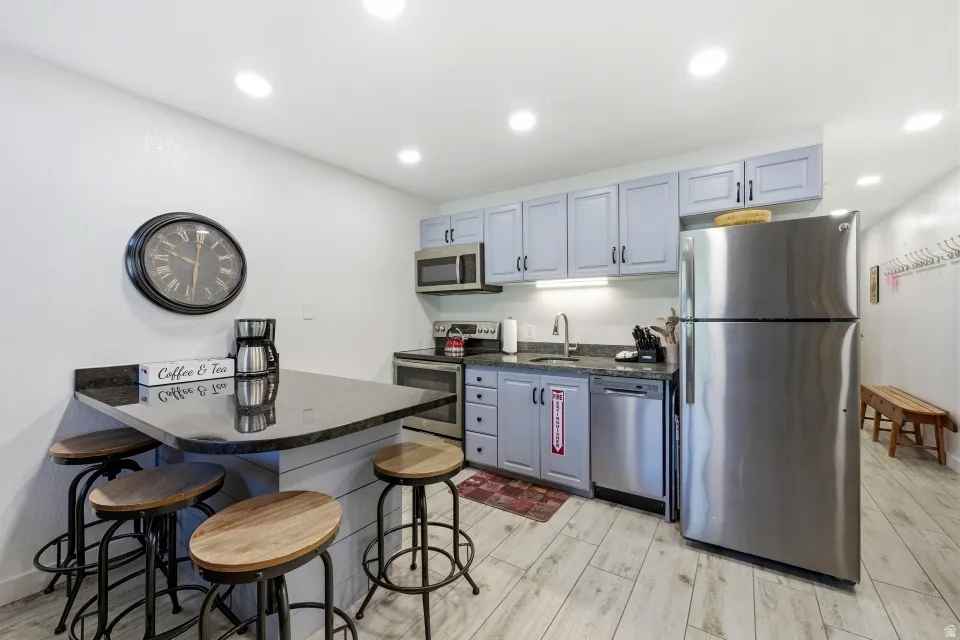 Kitchen with a kitchen bar, stainless steel appliances, light wood-style flooring, dark stone countertops, and recessed lighting