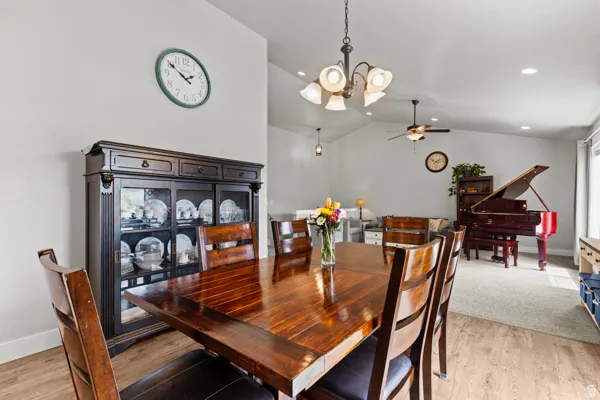 Dining room featuring a chandelier, light wood-style floors, vaulted ceiling, and ceiling fan