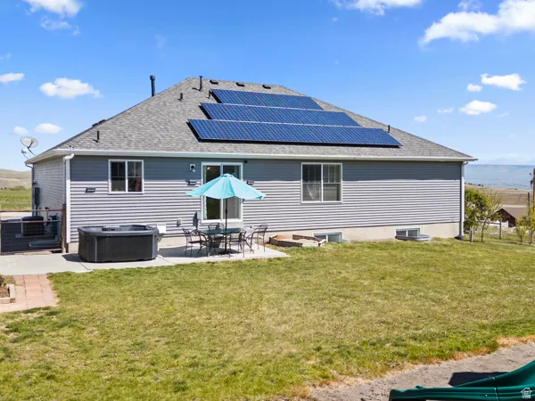 Rear view of house with solar panels, a hot tub, a yard, and a patio area