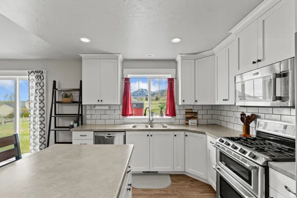 Kitchen with stainless steel appliances, white cabinetry, light wood-style flooring, light countertops, and backsplash