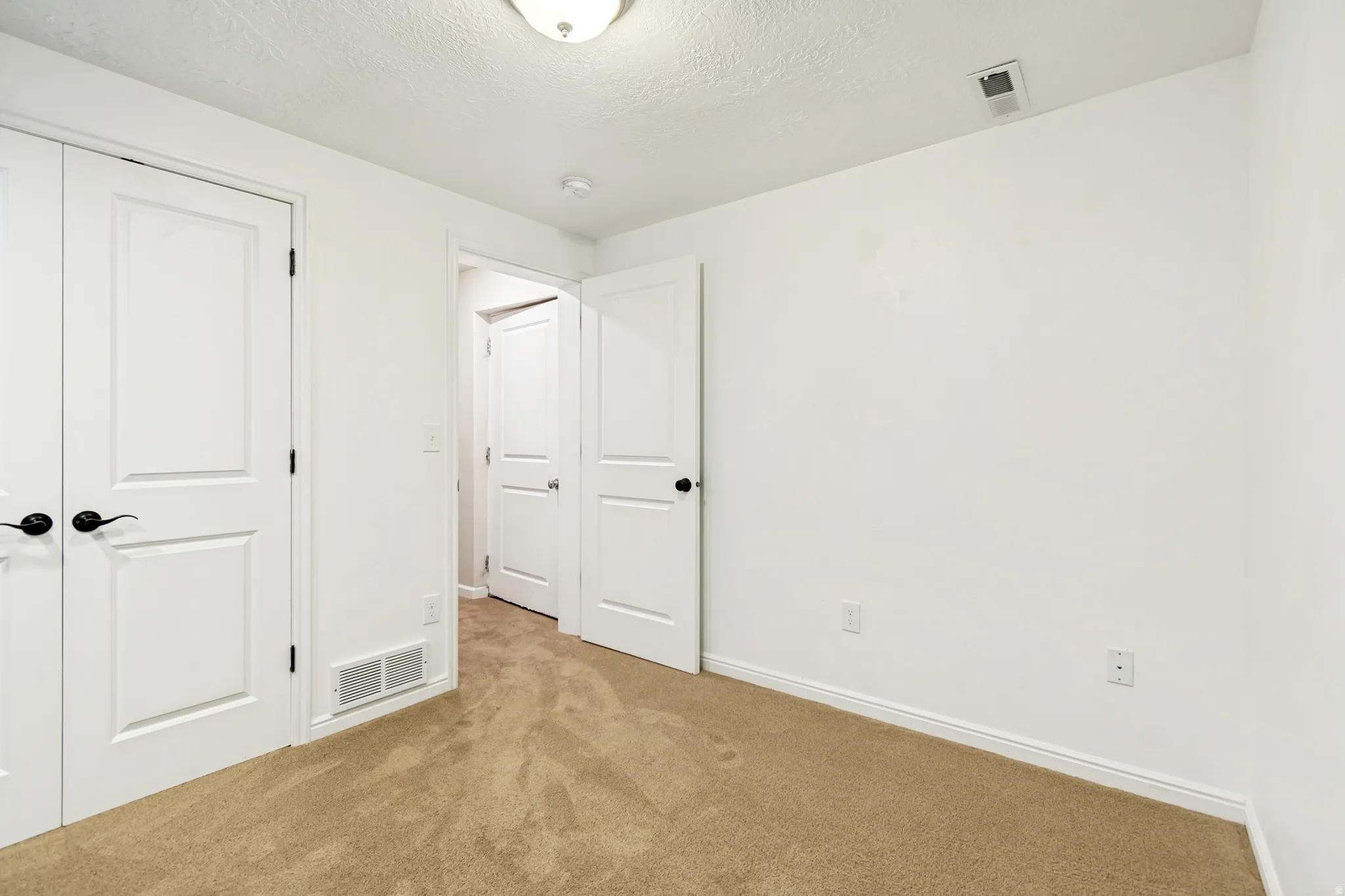 Unfurnished bedroom with a textured ceiling, a closet, and light carpet