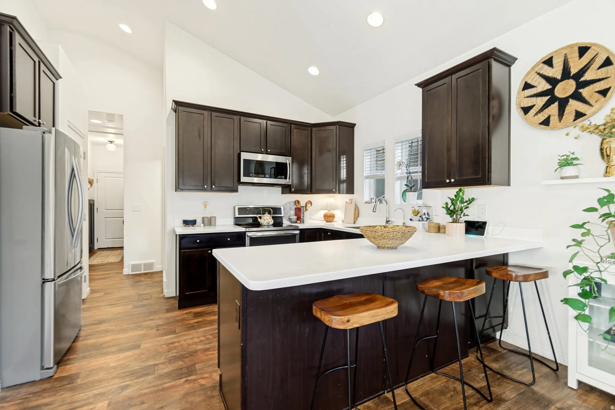 Kitchen featuring stainless steel appliances, a kitchen bar, dark wood finish cabinets, lofted ceiling, and a peninsula