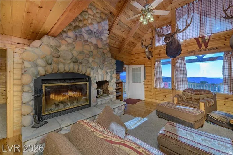 Living room with a stone fireplace, wood finished floors, a high wood beamed ceiling, wooden walls, and ceiling fan