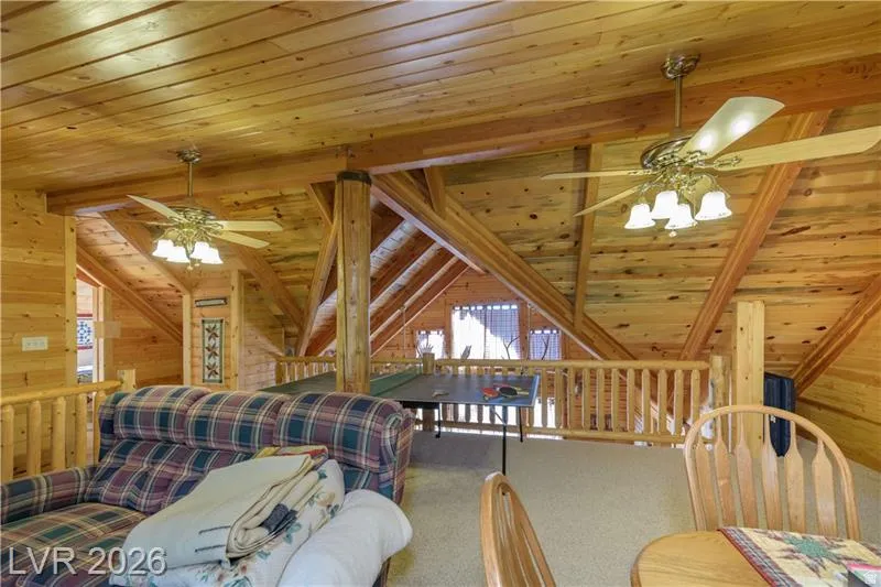 Carpeted bedroom with wood ceiling, vaulted ceiling with beams, wooden walls, and a ceiling fan