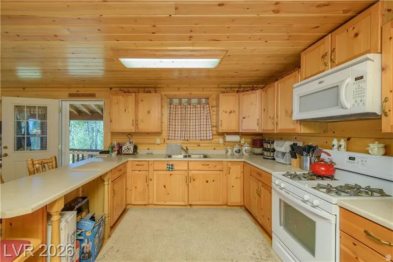 Kitchen with white appliances, light countertops, a peninsula, light wood finish cabinets, and wood ceiling