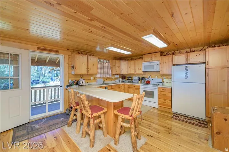 Kitchen with white appliances, light wood finished floors, light wood finish cabinetry, light countertops, and a peninsula