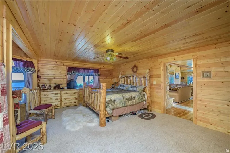 Bedroom featuring light colored carpet, wood ceiling, wooden walls, and ceiling fan