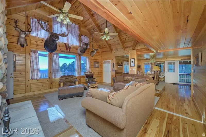 Living area featuring light wood-style flooring, a high wood beamed ceiling, wood walls, and a ceiling fan