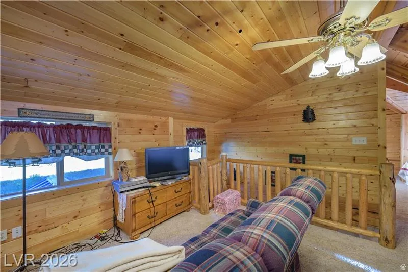 Carpeted living area featuring wooden walls, a vaulted wooden ceiling, and a ceiling fan