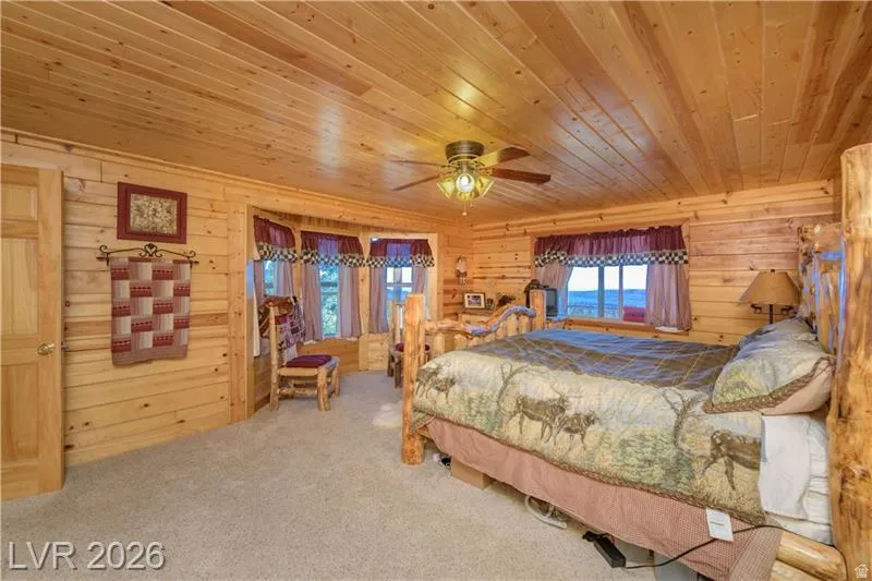 Bedroom with wood ceiling, light colored carpet, wooden walls, and a ceiling fan