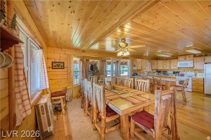 Dining space with light wood-type flooring, wooden ceiling, ceiling fan, and wooden walls