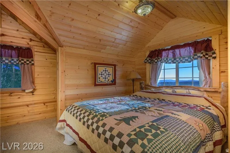 Carpeted bedroom with wood walls and a wooden ceiling with exposed beams