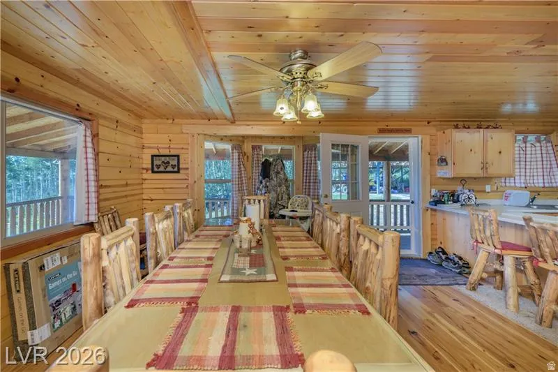 Dining space featuring healthy amount of natural light, light wood-style floors, wooden walls, wooden ceiling, and a ceiling fan
