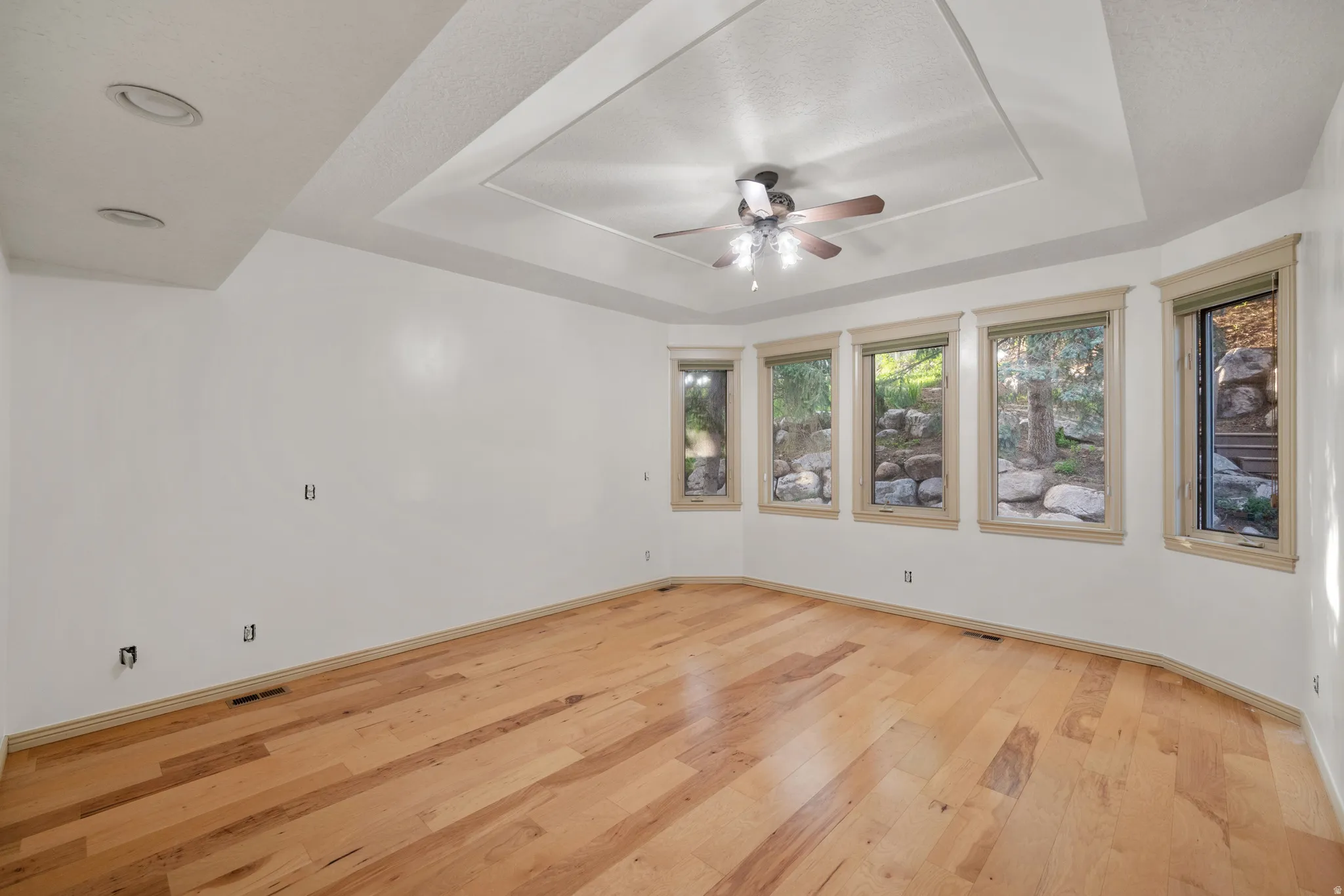 Primary Bedroom featuring light wood finished floors, a raised ceiling, and a ceiling fan. Look at those windows!