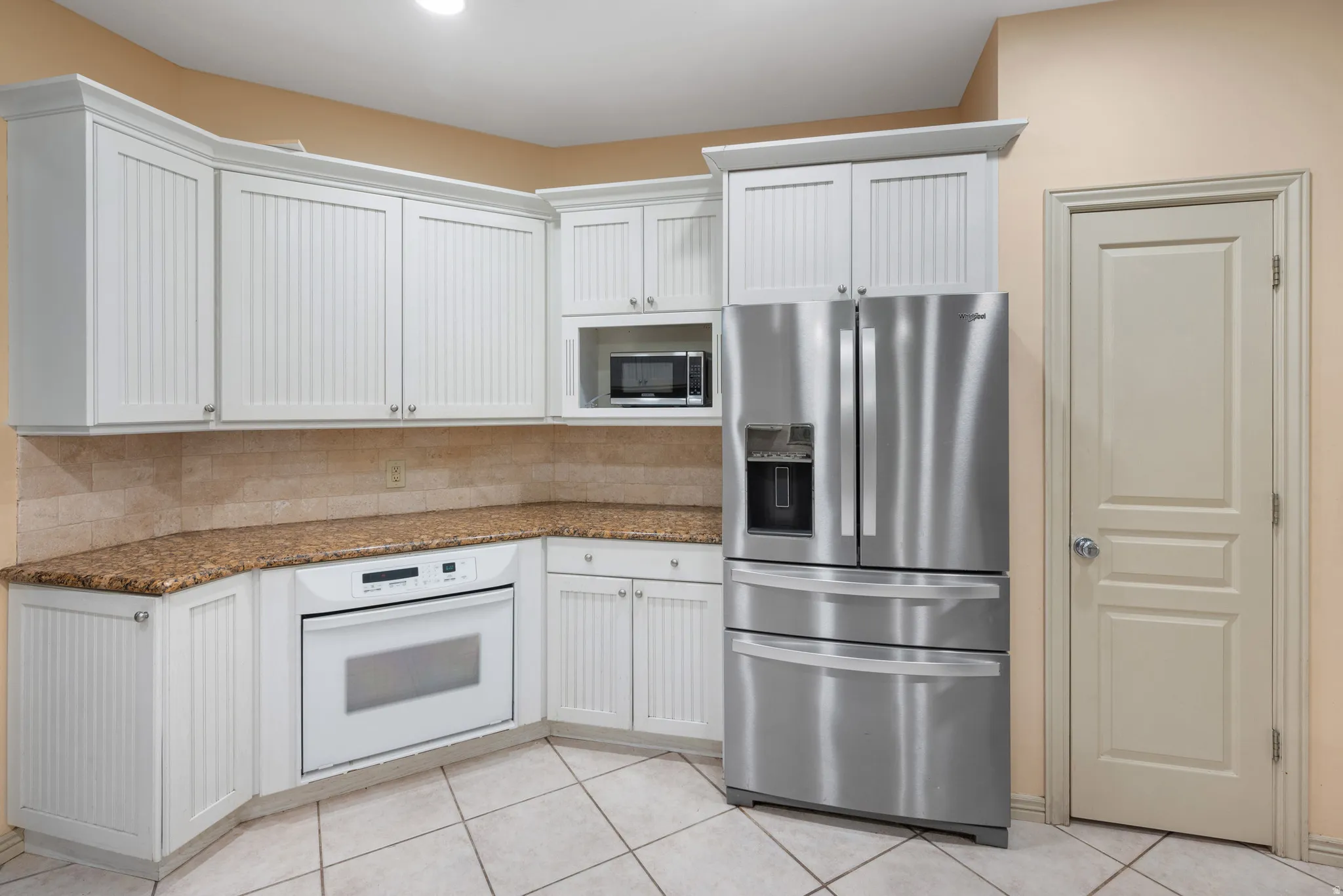 Kitchen featuring stainless steel appliances, dark stone countertops, white cabinets, light tile patterned floors, and backsplash