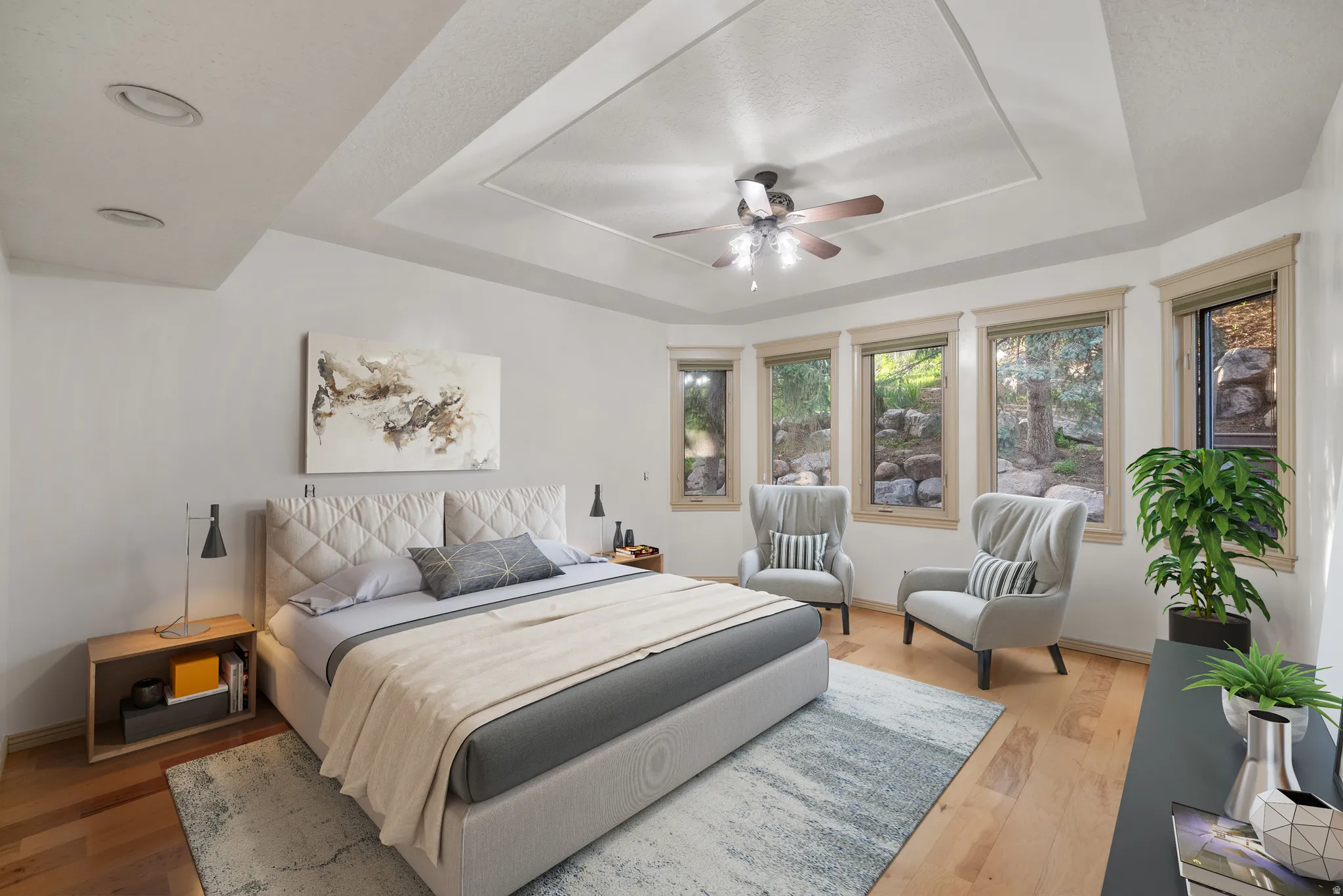 Virtually staged Primary Bedroom featuring light wood finished floors, a raised ceiling, and a ceiling fan. Look at those windows!