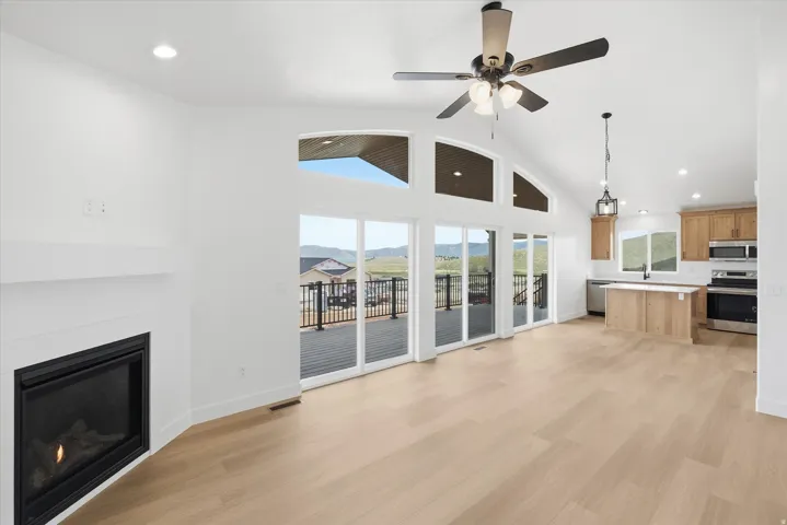Unfurnished living room featuring recessed lighting, a high ceiling, a glass covered fireplace, light wood finished floors, and ceiling fan