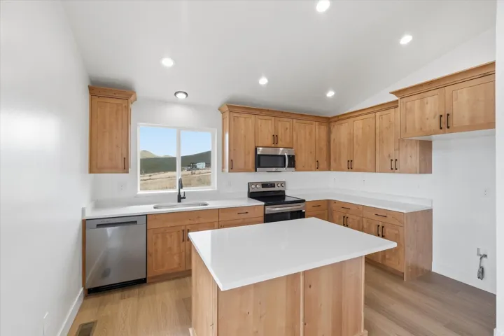 Kitchen with stainless steel appliances, a kitchen island, light wood finished floors, lofted ceiling, and recessed lighting