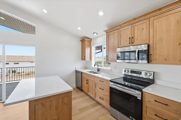 Kitchen with stainless steel appliances, light wood-type flooring, a center island, recessed lighting, and light stone countertops