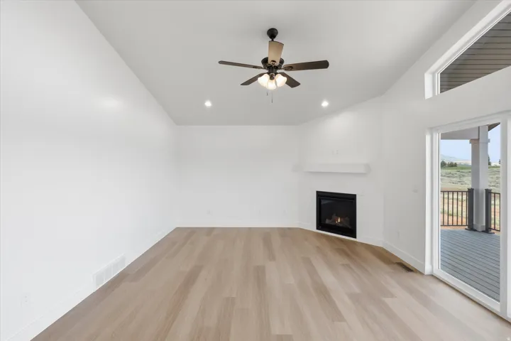 Unfurnished living room with light wood-type flooring, a glass covered fireplace, ceiling fan, recessed lighting, and vaulted ceiling