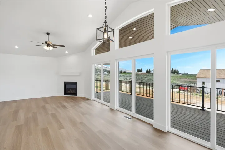Unfurnished living room with a glass covered fireplace, lofted ceiling, light wood-style flooring, recessed lighting, and a ceiling fan