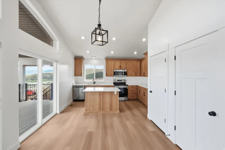 Kitchen featuring a kitchen island, light wood-style flooring, stainless steel appliances, hanging light fixtures, and wood finish cabinetry