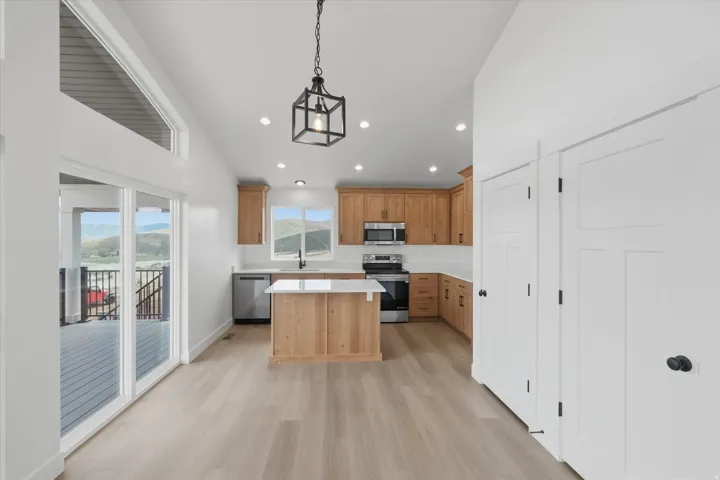 Kitchen with a center island, vaulted ceiling, stainless steel appliances, light wood-style floors, and decorative light fixtures