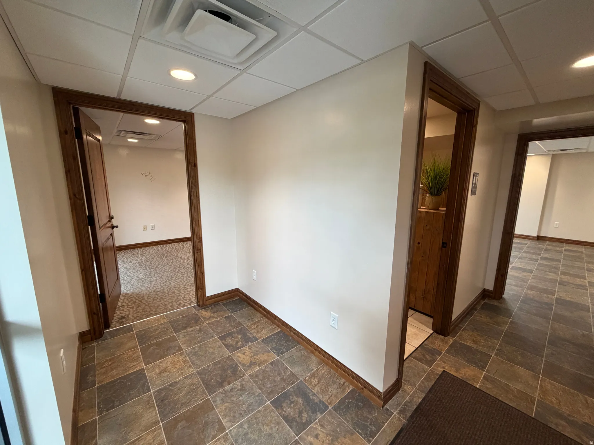 Hallway featuring a drop ceiling, dark stone finish flooring, and recessed lighting