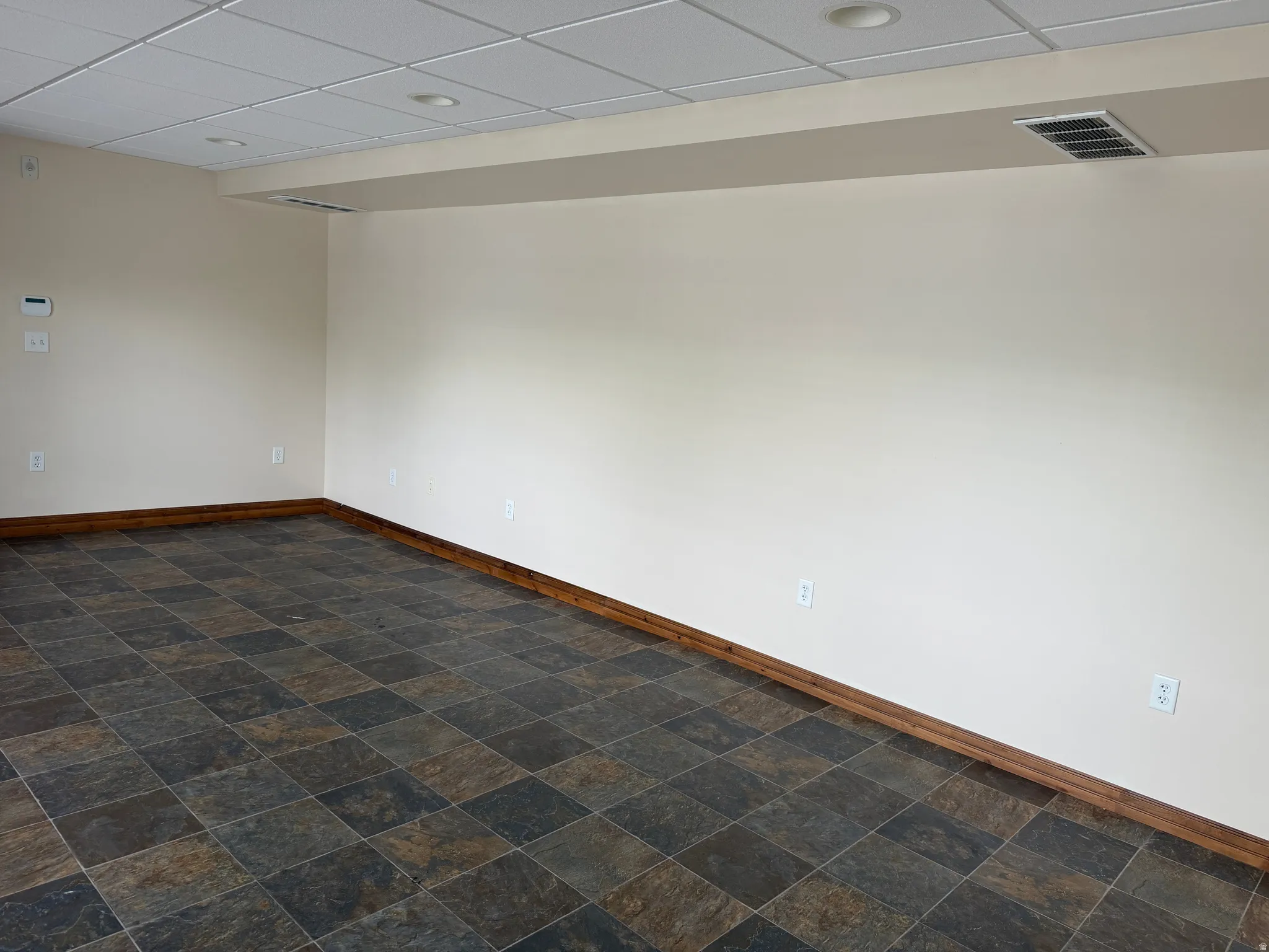 Unfurnished room featuring a paneled ceiling and dark stone finish flooring