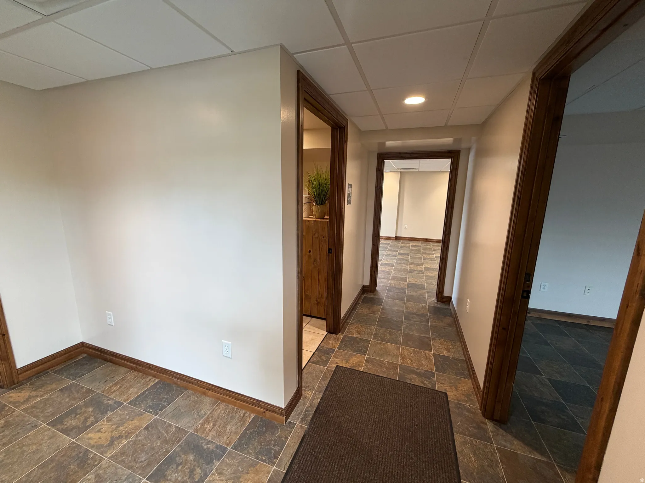 Hallway featuring a drop ceiling, dark stone finish floors, and recessed lighting