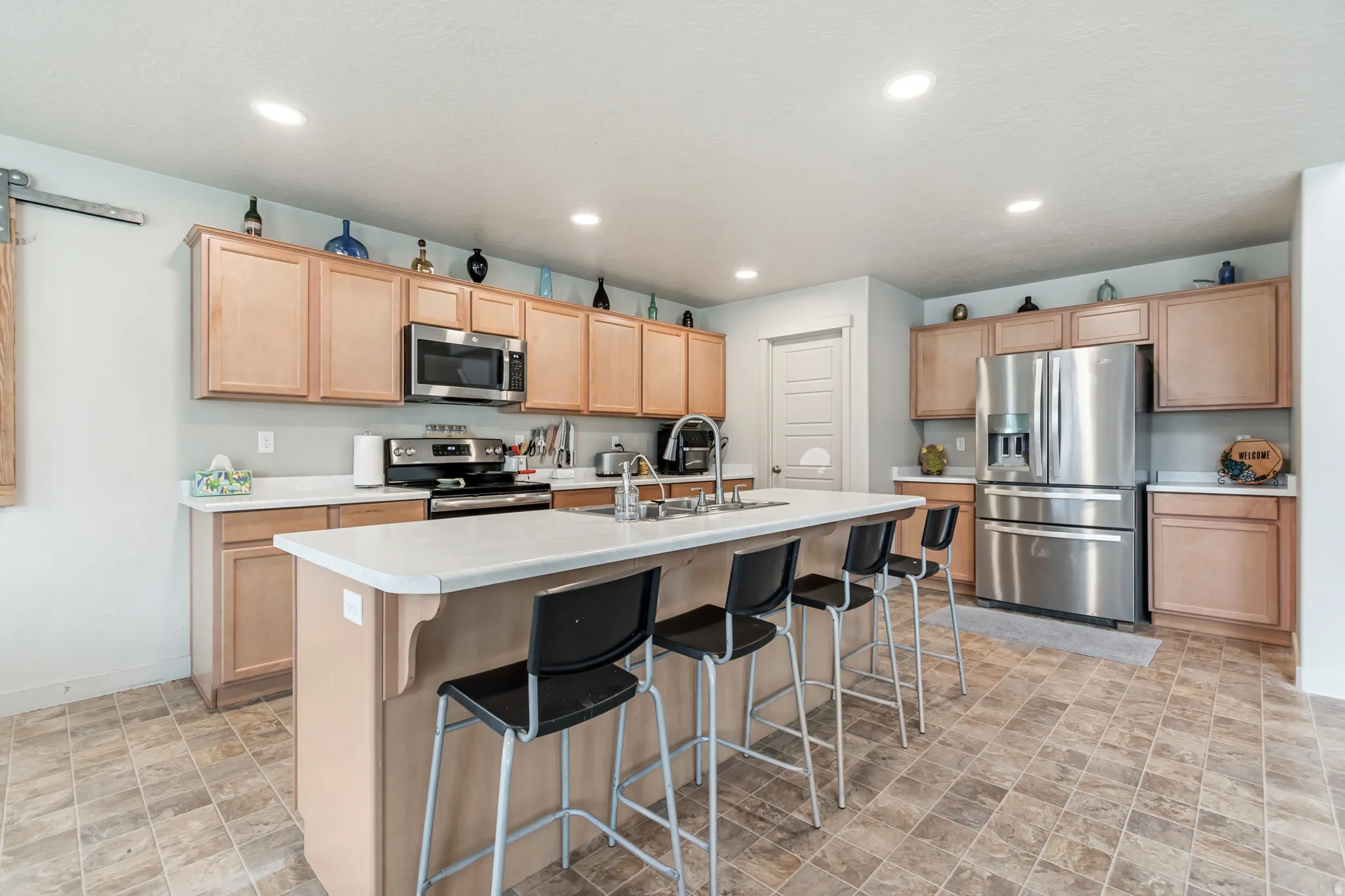 Kitchen with light countertops, stainless steel appliances, a breakfast bar area, an island with sink, and light wood finish cabinetry