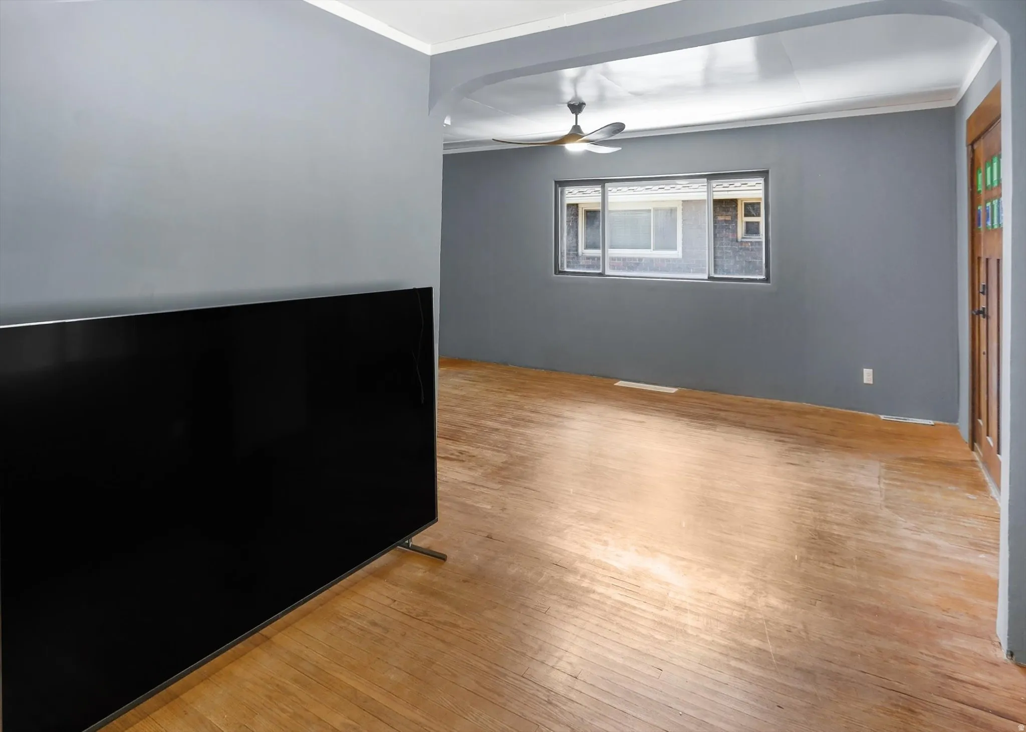 Spare room with arched walkways, crown molding, light wood-style floors, and a ceiling fan