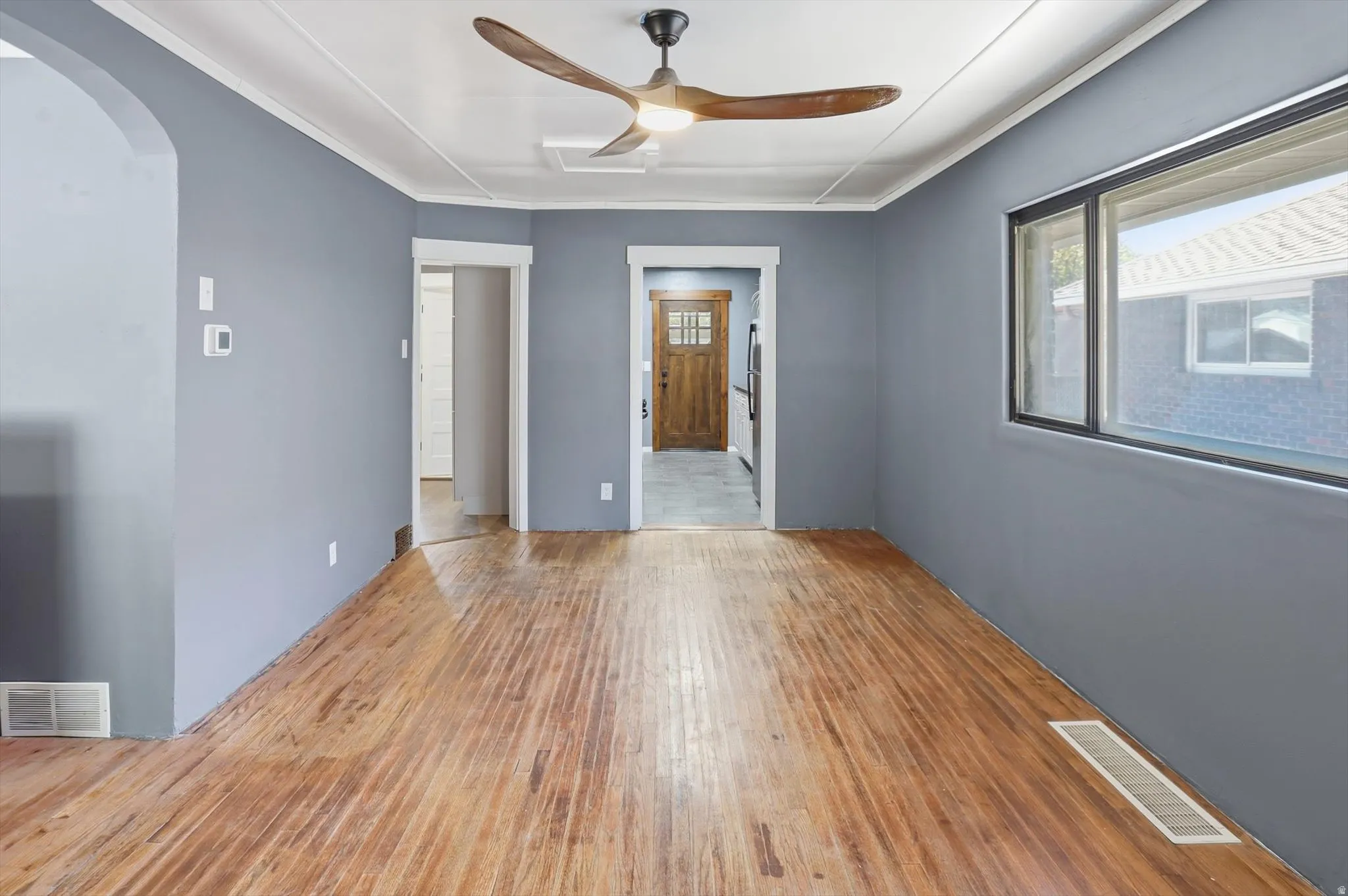 Spare room featuring arched walkways, light wood-type flooring, a ceiling fan, and ornamental molding