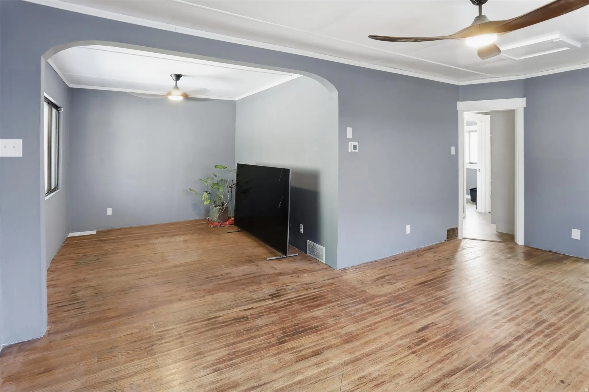 Empty room featuring a ceiling fan, arched walkways, crown molding, and light wood-style floors
